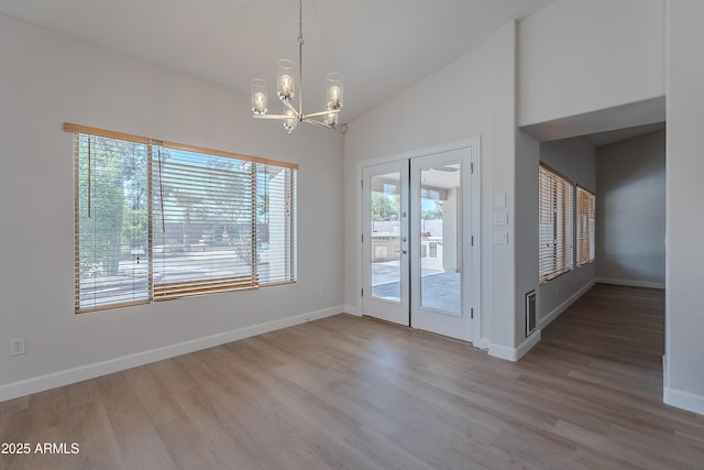unfurnished dining area with a wealth of natural light, wood finished floors, an inviting chandelier, and french doors