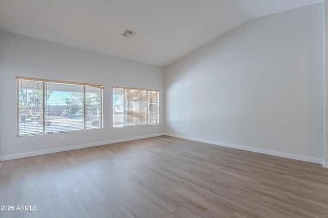 unfurnished room with baseboards, visible vents, wood finished floors, and lofted ceiling