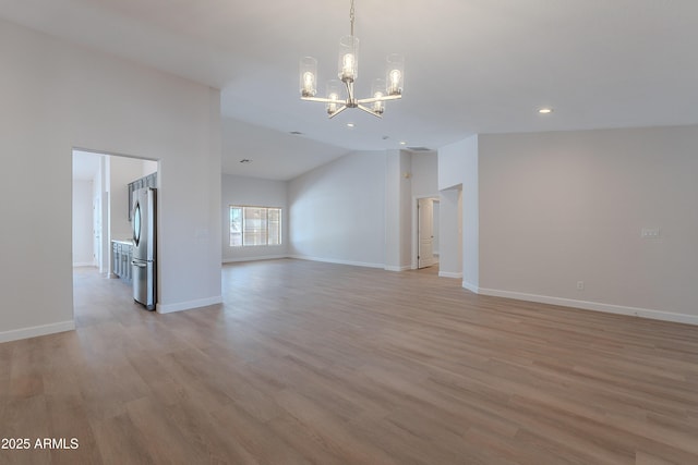 unfurnished room with light wood finished floors, a notable chandelier, vaulted ceiling, and baseboards