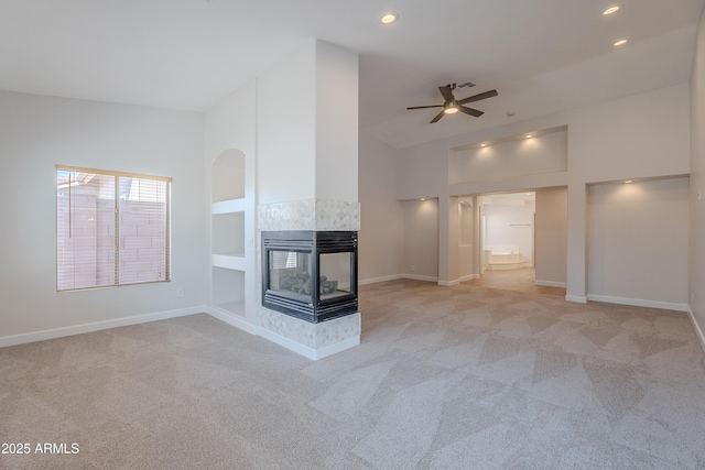 unfurnished living room featuring a ceiling fan, baseboards, a multi sided fireplace, and light carpet