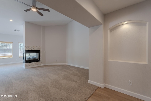 unfurnished living room featuring a multi sided fireplace, visible vents, baseboards, wood finished floors, and a ceiling fan