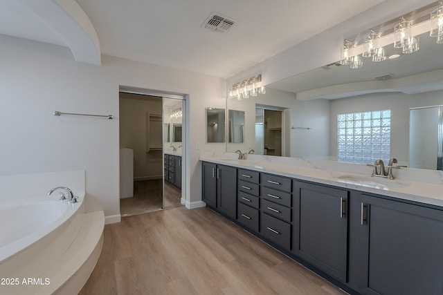 bathroom with a sink, double vanity, visible vents, a garden tub, and wood finished floors