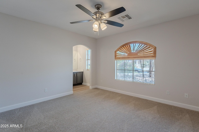 unfurnished room featuring light colored carpet, visible vents, arched walkways, and baseboards