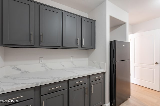 kitchen with light stone counters, gray cabinets, freestanding refrigerator, and light wood-type flooring