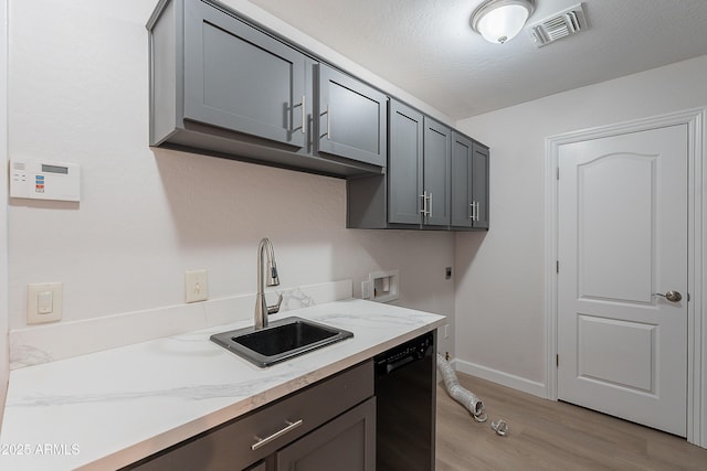 kitchen featuring a sink, light wood-style floors, black dishwasher, visible vents, and baseboards