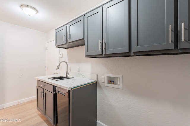 laundry area with washer hookup, a sink, baseboards, light wood finished floors, and cabinet space