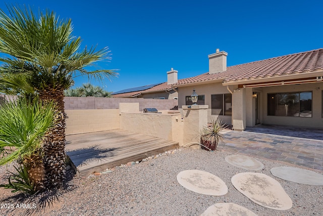 rear view of house featuring a tile roof, a patio, fence private yard, a chimney, and stucco siding