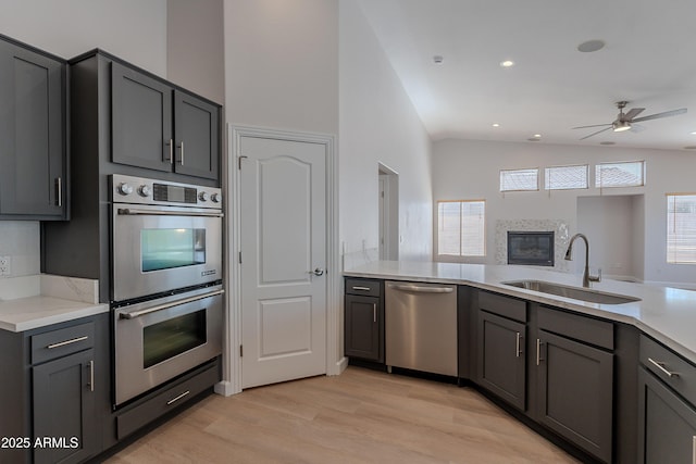 kitchen with gray cabinetry, stainless steel appliances, vaulted ceiling, and a sink