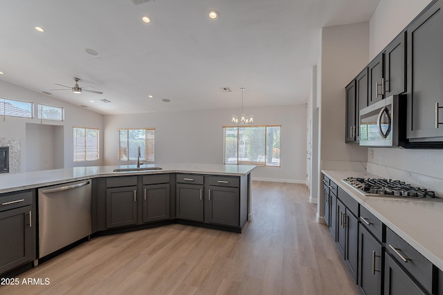 kitchen with a sink, stainless steel appliances, light countertops, light wood-type flooring, and ceiling fan with notable chandelier