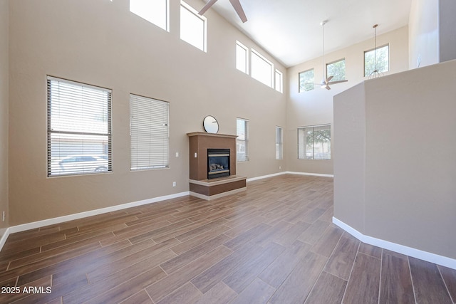 125 N 22nd Pl Unit 14, Mesa, AZ 85213 - unfurnished living room featuring ceiling fan, wood finished floors, a high ceiling, baseboards, and a glass covered fireplace