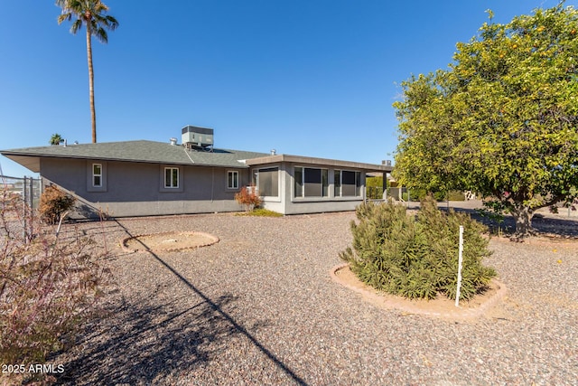 rear view of property with stucco siding, fence, central AC unit, and a sunroom