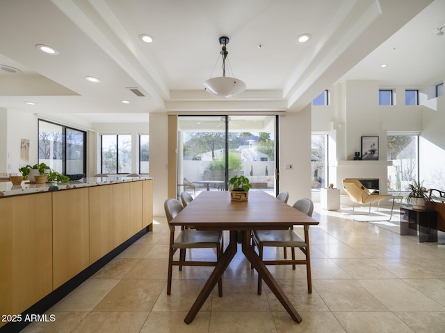 dining room with a raised ceiling, a glass covered fireplace, visible vents, and recessed lighting