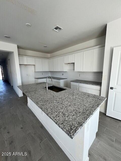 kitchen with dark wood-type flooring, sink, a center island with sink, dark stone countertops, and white cabinets