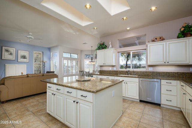 kitchen featuring a skylight, sink, white cabinets, dark stone counters, and stainless steel dishwasher