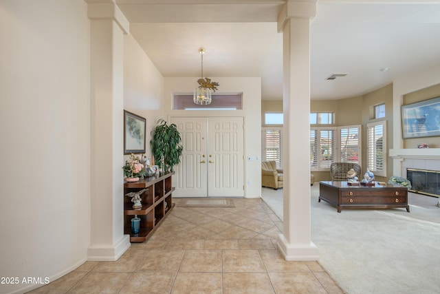 foyer featuring a tiled fireplace, decorative columns, and light tile patterned floors