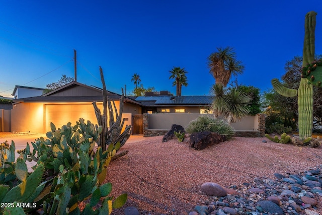 ranch-style home featuring stucco siding, solar panels, fence, and an attached garage
