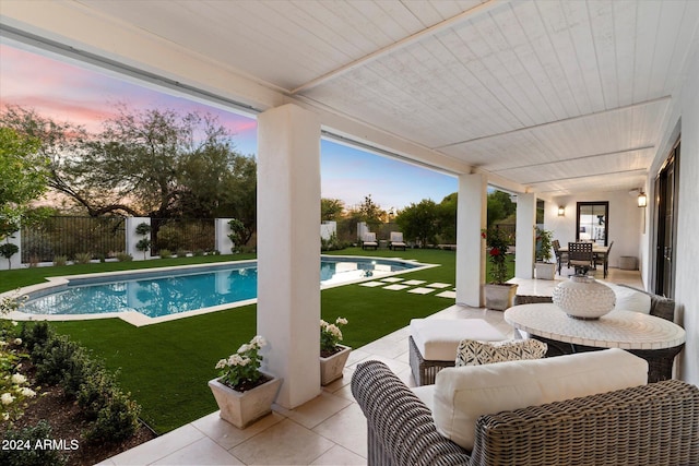 pool at dusk featuring an outdoor living space, a patio, and a lawn