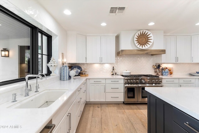 kitchen with light wood-type flooring, custom range hood, sink, range with two ovens, and white cabinetry