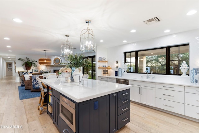 kitchen featuring sink, light hardwood / wood-style floors, a center island with sink, white cabinets, and appliances with stainless steel finishes