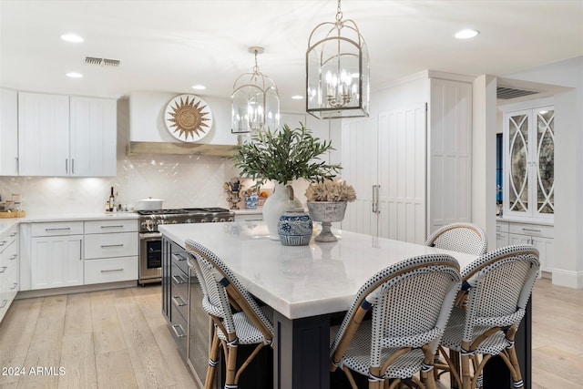 kitchen with decorative light fixtures, a kitchen island, high end stainless steel range oven, and light hardwood / wood-style flooring