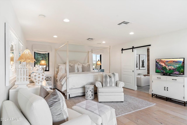 bedroom featuring light wood-type flooring, a barn door, ensuite bathroom, and multiple windows