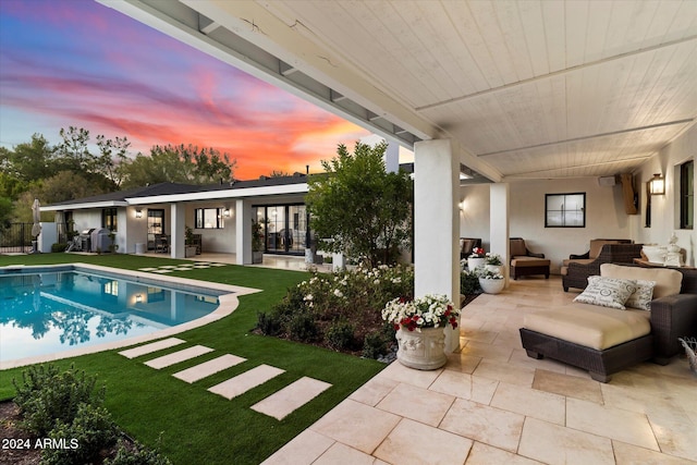 pool at dusk featuring an outdoor living space, a patio area, and a lawn