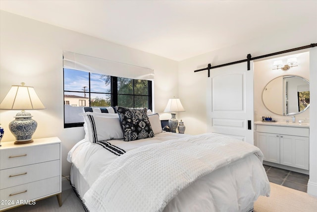 bedroom with tile patterned floors, a barn door, ensuite bath, and sink