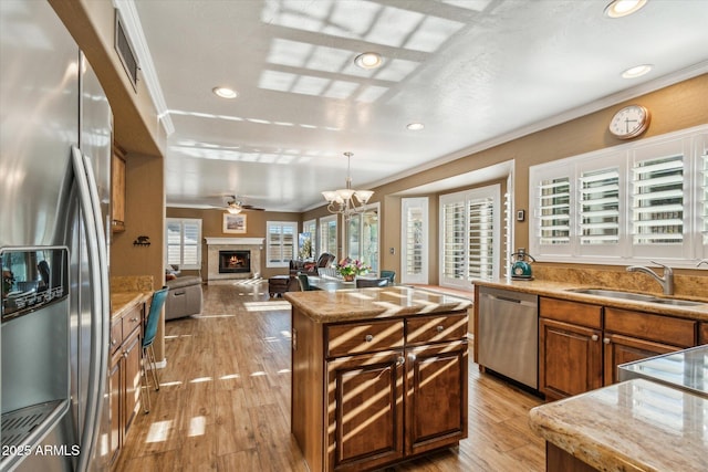 kitchen with sink, pendant lighting, a kitchen island, stainless steel appliances, and ornamental molding