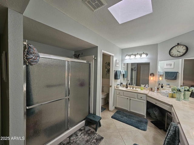 bathroom featuring a skylight, tile patterned floors, an enclosed shower, a textured ceiling, and toilet