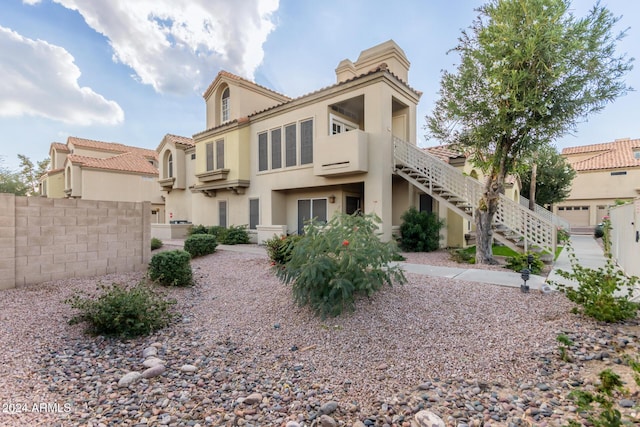 view of front of home featuring a tiled roof, fence, stairway, and stucco siding