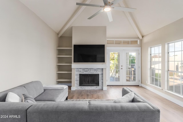 living room with beam ceiling, a stone fireplace, wood finished floors, and french doors