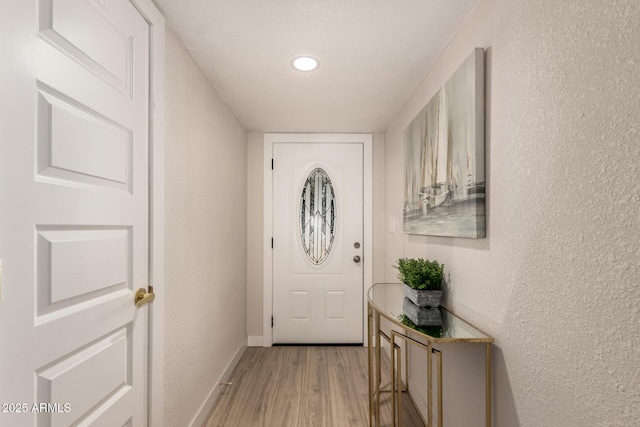 doorway with a textured wall, baseboards, light wood-style floors, and recessed lighting