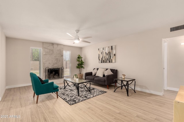 living room with baseboards, light wood finished floors, ceiling fan, visible vents, and a tile fireplace