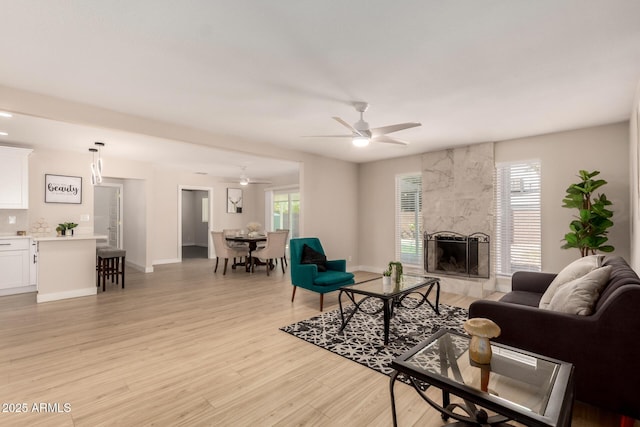 living area featuring baseboards, ceiling fan, a tiled fireplace, and light wood-type flooring