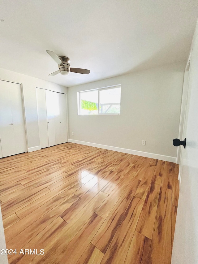 unfurnished bedroom with two closets, ceiling fan, and light hardwood / wood-style floors