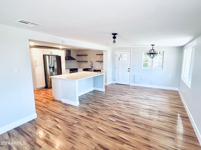 kitchen with a kitchen island, stainless steel fridge, wall chimney exhaust hood, a fireplace, and light wood-type flooring