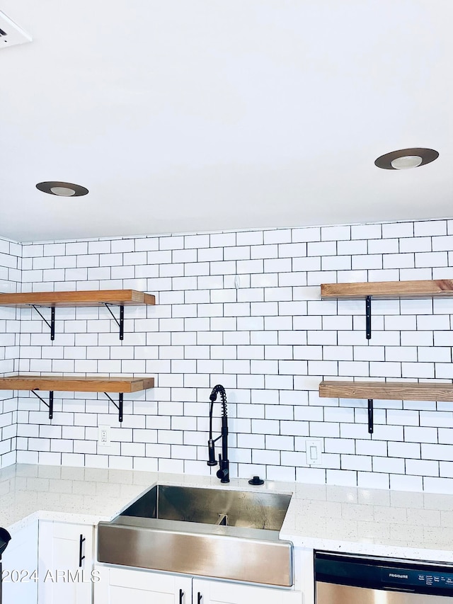 kitchen with stainless steel dishwasher, light stone counters, white cabinetry, and sink