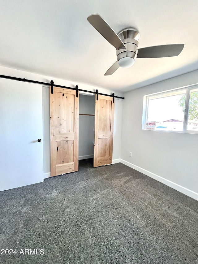 unfurnished bedroom featuring a barn door, ceiling fan, and carpet