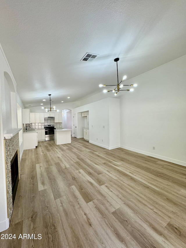 unfurnished living room featuring a textured ceiling, a notable chandelier, a fireplace, visible vents, and light wood-style floors