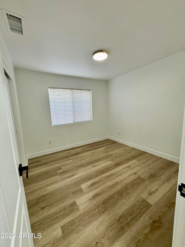 empty room featuring wood finished floors, visible vents, and baseboards