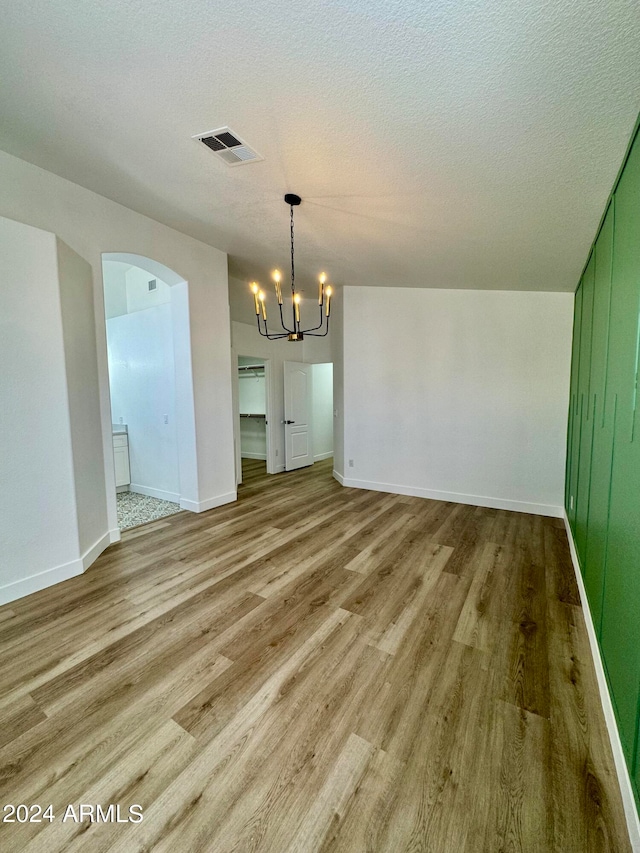 unfurnished dining area with a chandelier, arched walkways, visible vents, and wood finished floors