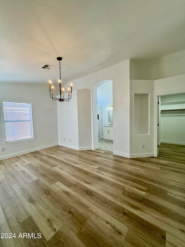 unfurnished dining area with light wood-type flooring, visible vents, arched walkways, and a textured ceiling