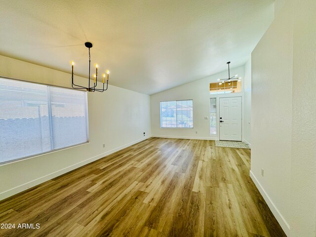 unfurnished dining area featuring lofted ceiling, an inviting chandelier, baseboards, and wood finished floors