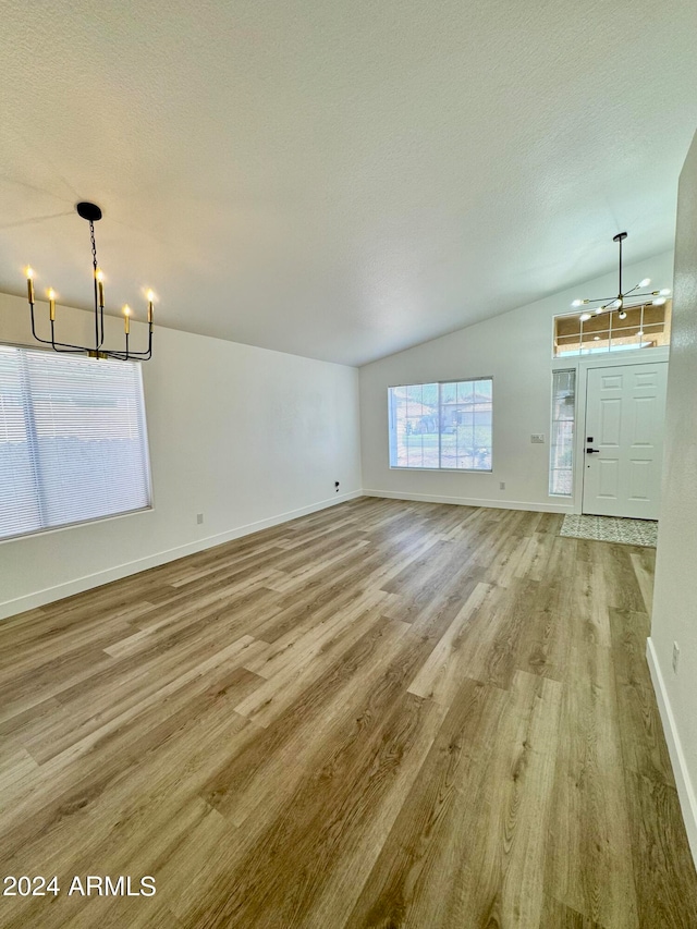 unfurnished living room with a textured ceiling, a notable chandelier, baseboards, vaulted ceiling, and light wood-type flooring