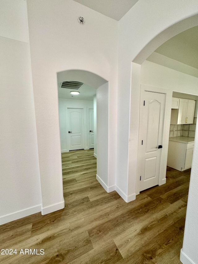 hallway featuring arched walkways, wood finished floors, visible vents, and baseboards