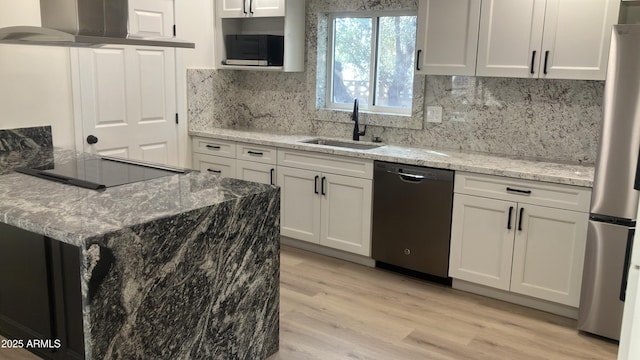 kitchen with a sink, wall chimney range hood, white cabinetry, black appliances, and light stone countertops