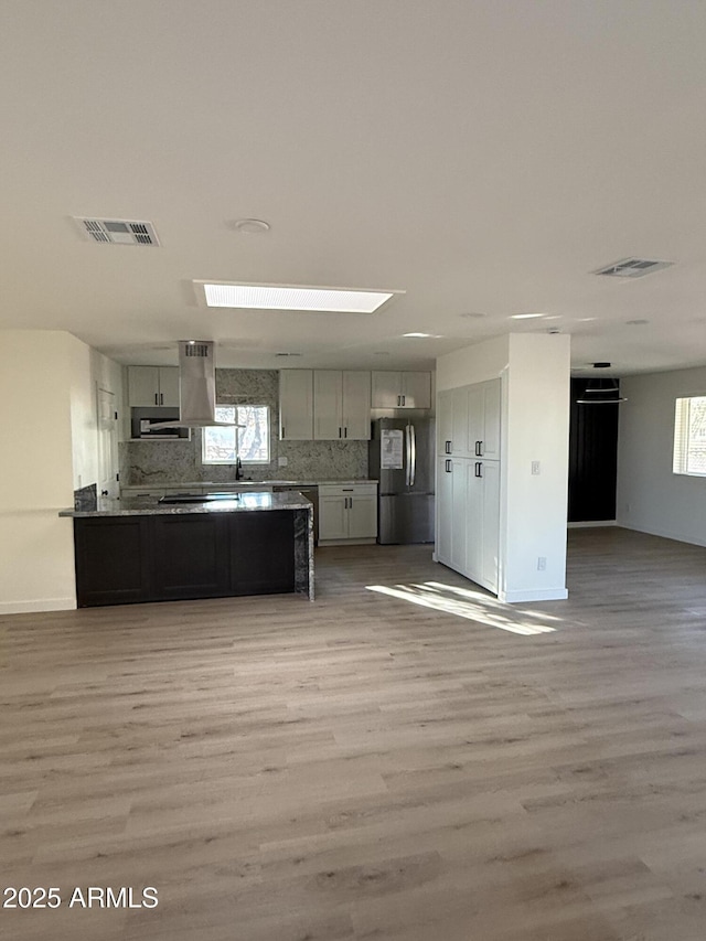 kitchen featuring visible vents, open floor plan, freestanding refrigerator, a peninsula, and island exhaust hood