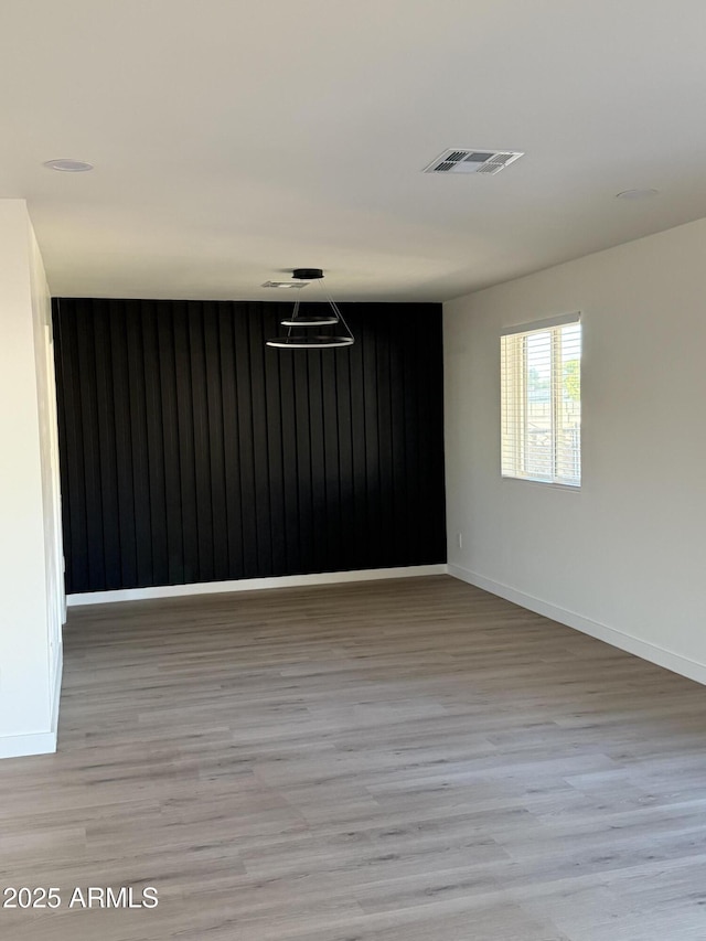 empty room with light wood-type flooring, visible vents, and baseboards