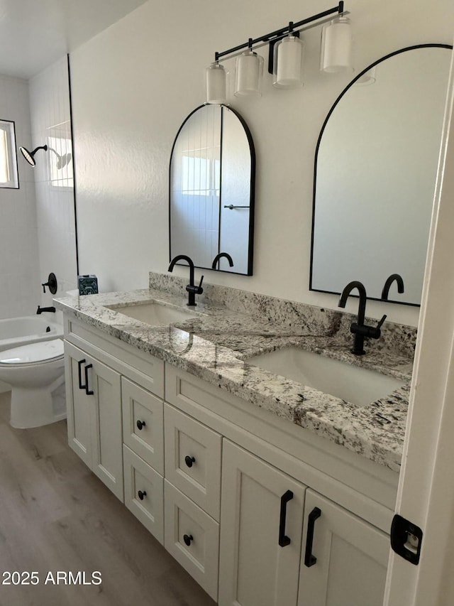 full bathroom with double vanity, wood finished floors, a sink, and bathing tub / shower combination