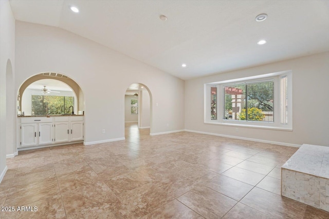 unfurnished living room featuring arched walkways, baseboards, and vaulted ceiling